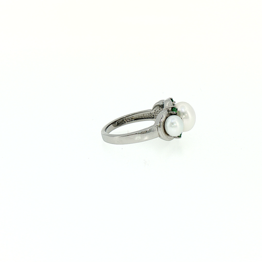 A silver ring featuring three white pearls and small green gemstones