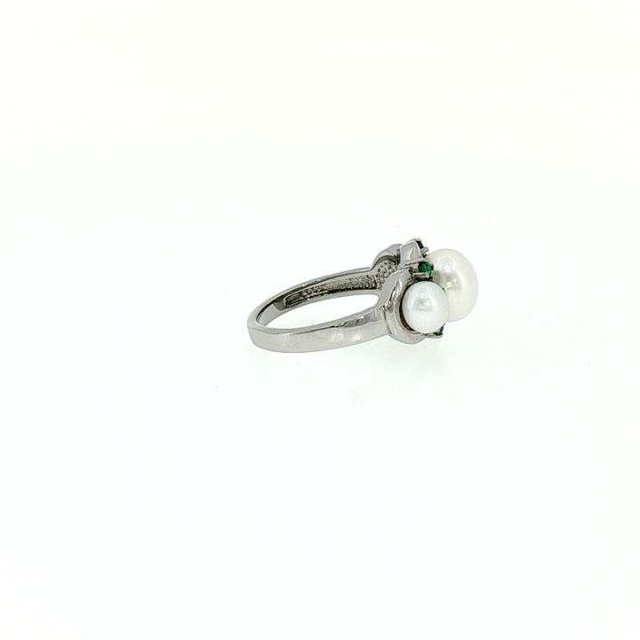 A silver ring featuring three white pearls and small green gemstones
