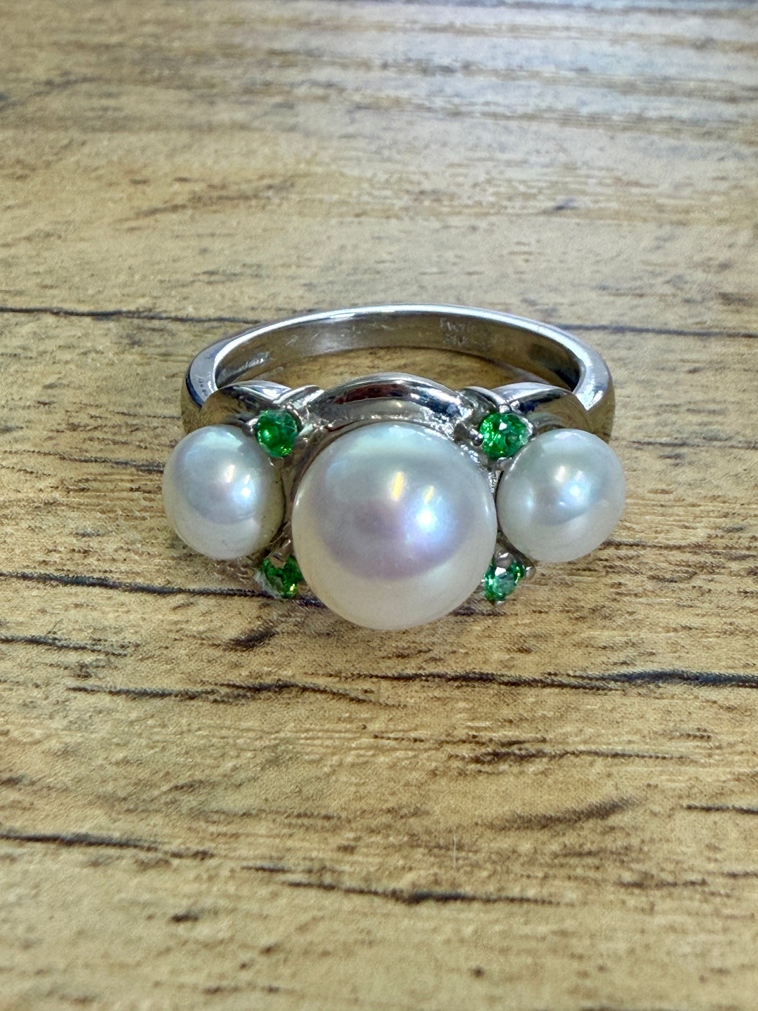 A silver ring featuring three white pearls and small green gemstones