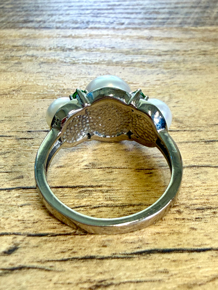 A silver ring featuring three white pearls and small green gemstones